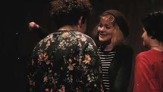 três pessoas aparecem no quadro, uma delas de costas com uma blusa florida. outra aparece de frente com uma touca e uma blusa listrada e a terceira pessoa aparece de perfil no lado direito da tela.