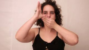 artista centralizada em fundo branco com a mão esquerda sobre a boca e o nariz e a mão direita sobre a orelha direita.