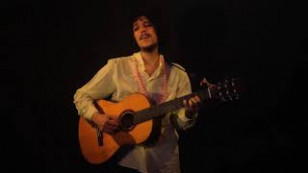 Musico com violão ao centro de um fundo escuro