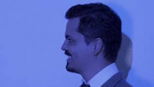 perfil do ator aparece no centro da imagem, sorrindo, de terno e gravata
