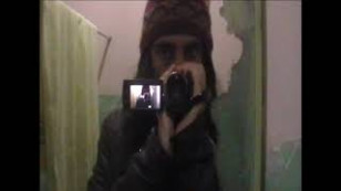 Homem aparece no centro com uma câmera na mão. Veste uma touca. Ao fundo, uma cortina de banheiro.jpg