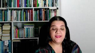 autora aparece em frente a uma estante de livros