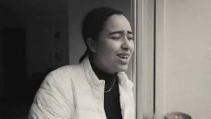 artista aparece ao centro em uma imagem em preto e branco, no fundo aparece um batente de porta