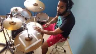 o musico aparece sentado tocando bateria