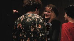 três pessoas aparecem no quadro, uma delas de costas com uma blusa florida. outra aparece de frente com uma touca e uma blusa listrada e a terceira pessoa aparece de perfil no lado direito da tela.