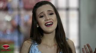 cantora aparece no centro gesticulando, o fundo é borrado.